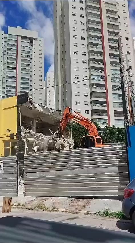 Demolição mecanizada da fachada, com o canteiro isolado por tapume